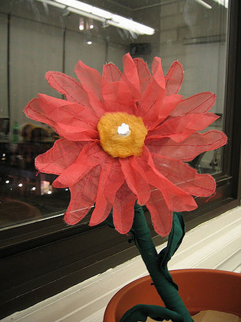 a fabric and wire flower with LEDs at the center sitting indoors on a windowsill at night