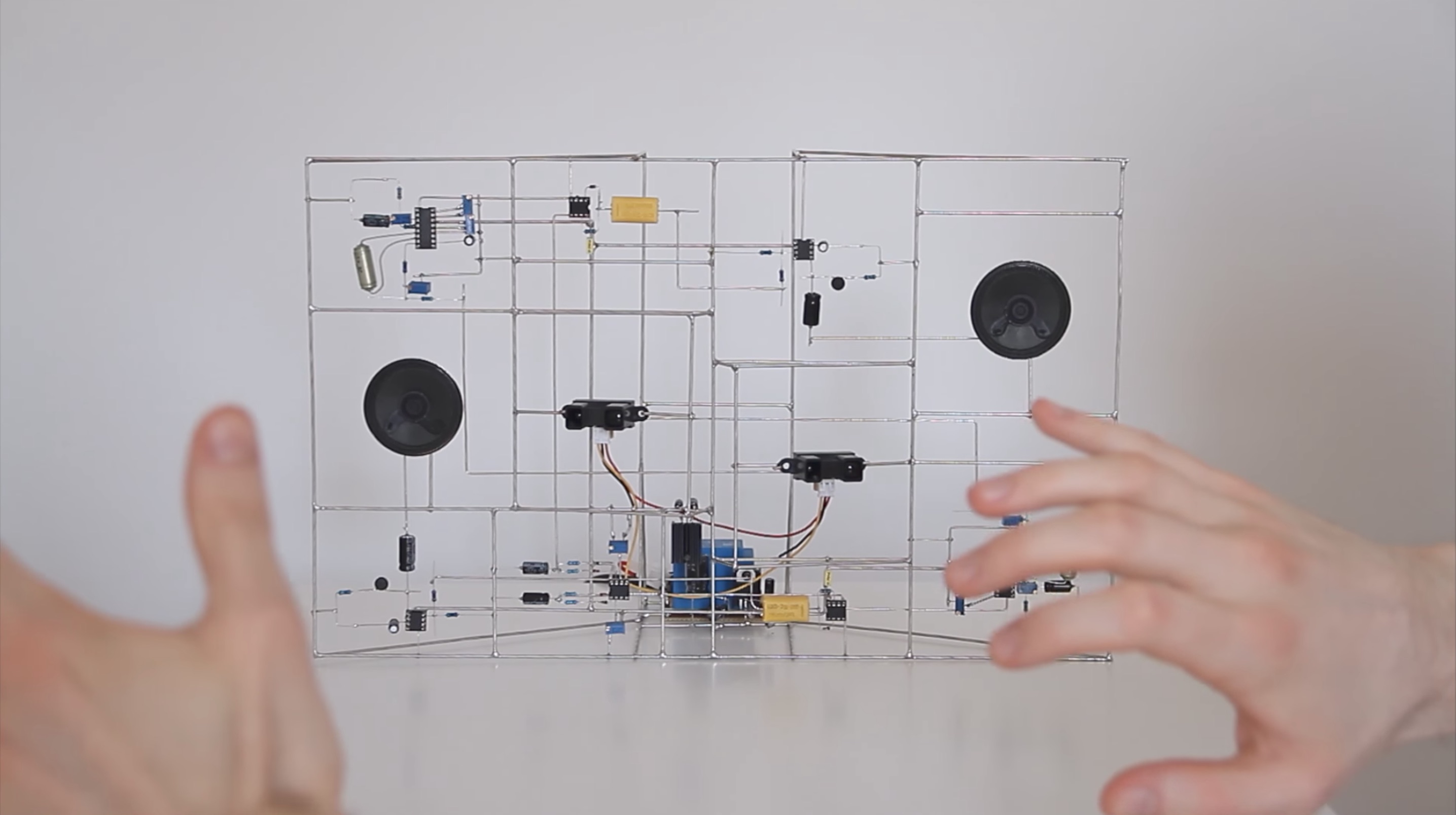 A circuit, but the wires are the structure instead of them being traces on the board. There are two speakers integrated in the structure, and hands in the foreground.