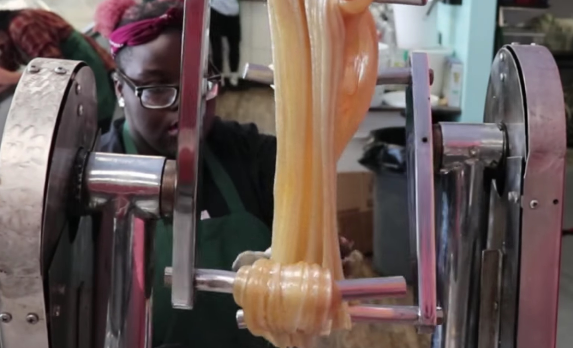 Woman watches as taffy-like warm sugar is spun on a machine turning it from clear to white