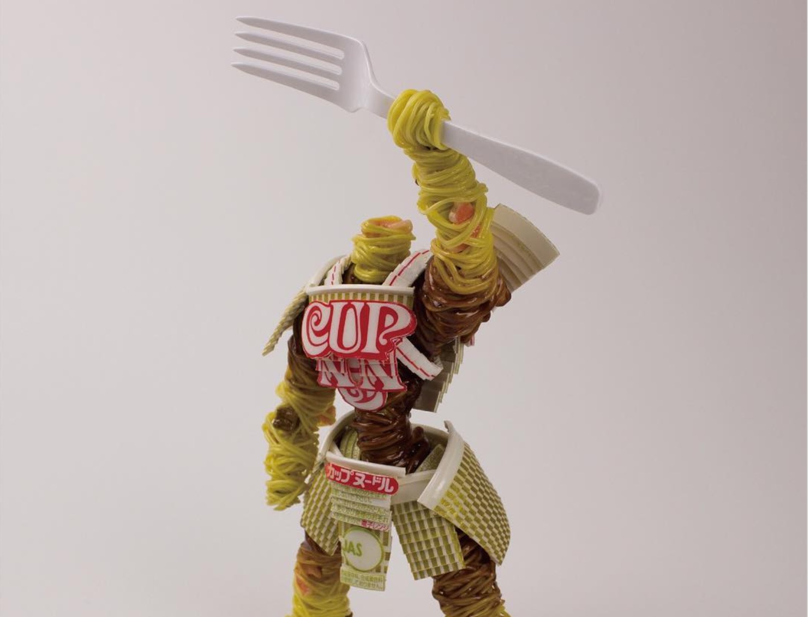 a tangle of noodles in the shape or a warrior wielding a fork overhead in defiance. Armor is made from cup-of-noddles packaging.