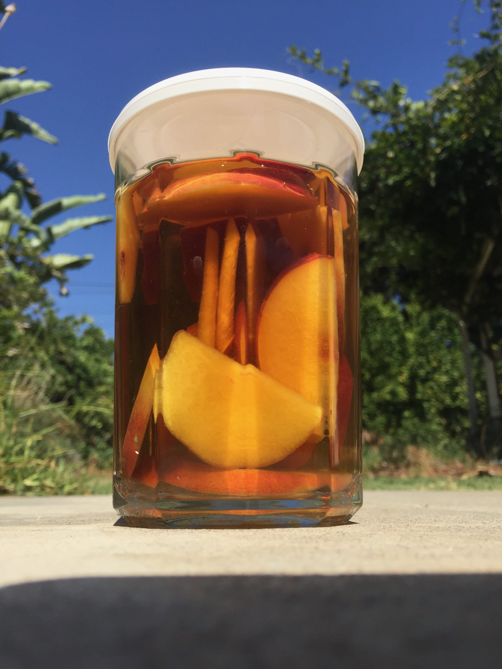 a glass of amber liquid with slices of peaches in it