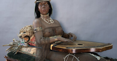 Isis A medium shot of the life-size Isis figure sitting oher cabinet with her zither on her lap and a mounted cat behind her