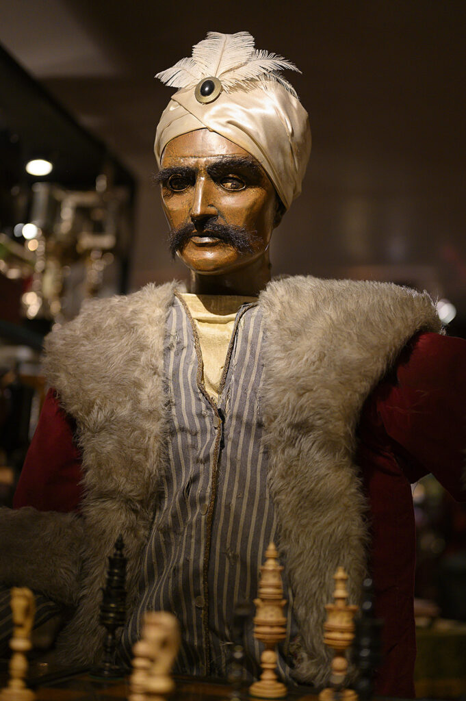 The Mechanical Turk - an image of the head and torso of The Turk, with pieces on the chess board visible in the fireground