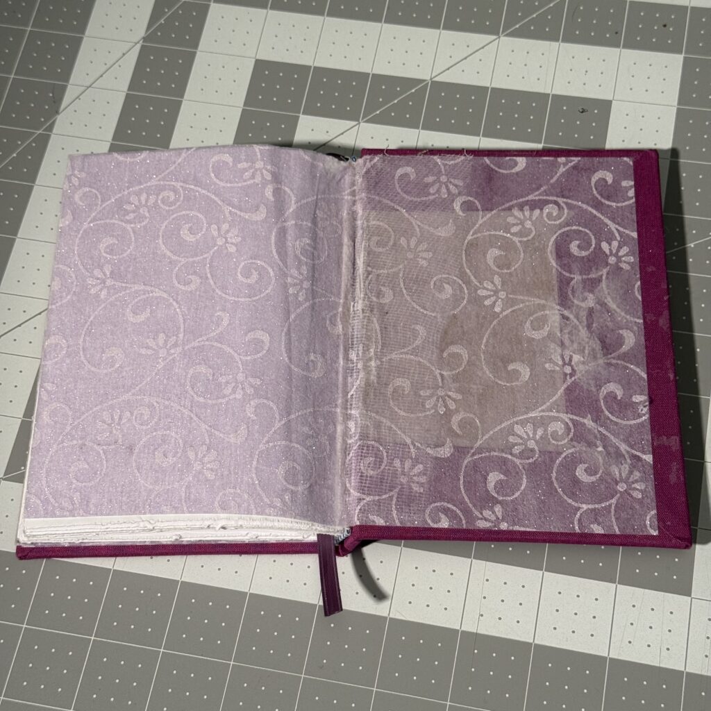 Hardcover book sitting on a gray cutting mat. The rear cover is opened, showing a sheer sparkly end paper. 
