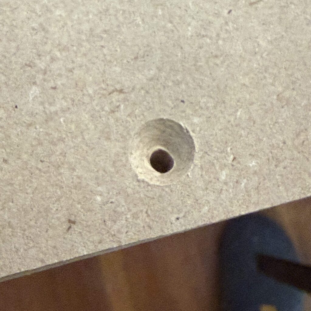 Close up image of countersunk hole for a screw to attach square stock to edge of MDF sheet.