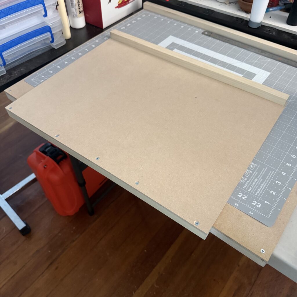 Completed bench hook, with a piece of square stock on top at the back of the MDF sheet, and another piece of square stock on the bottom front of the MDF sheet.
